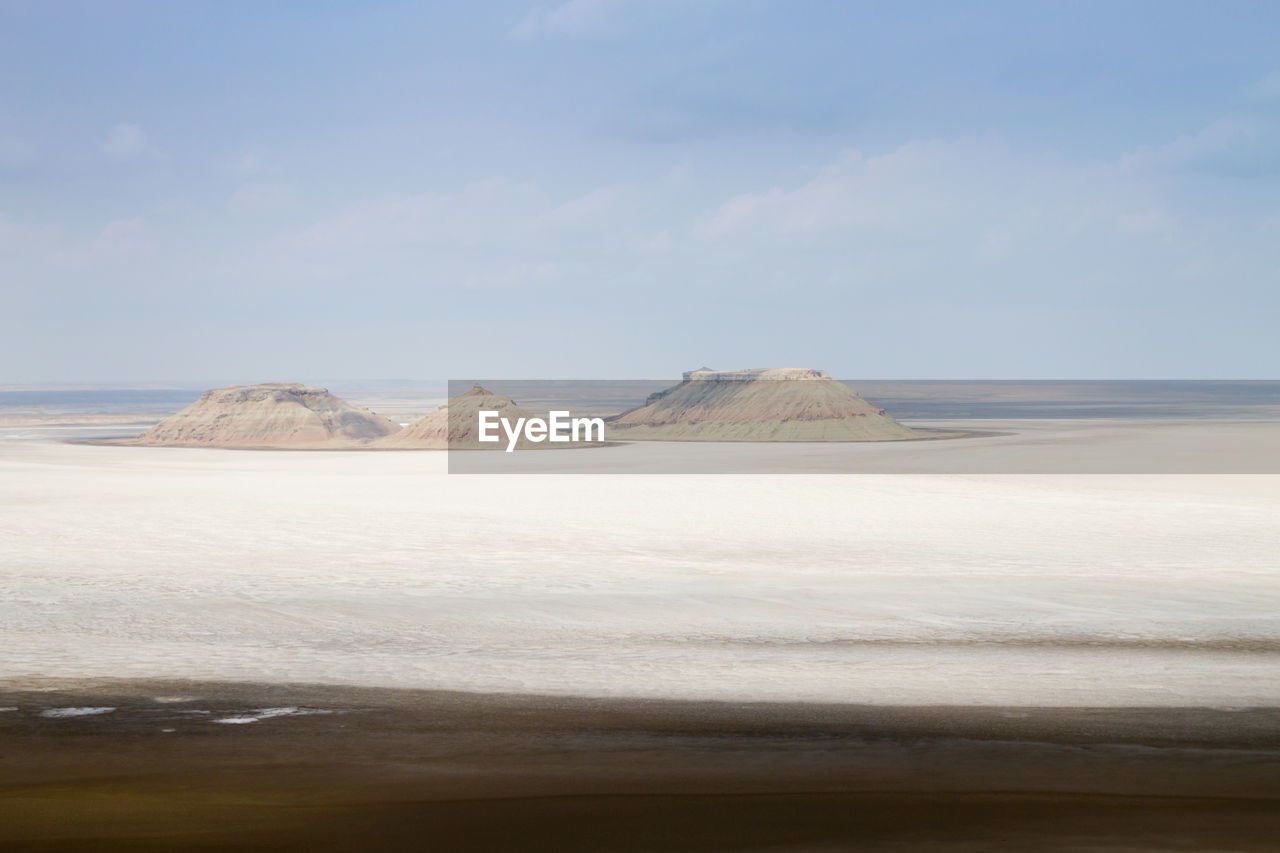 land, sky, natural environment, scenics - nature, beauty in nature, water, sand, sea, nature, environment, beach, landscape, tranquility, cloud, tranquil scene, day, coast, no people, shore, non-urban scene, travel destinations, body of water, horizon, desert, outdoors, travel, ocean, remote, tourism, idyllic, blue, mineral