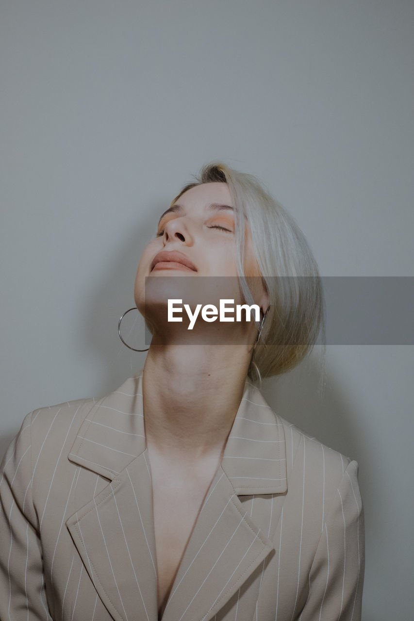 Close-up of young woman wearing blazer against wall