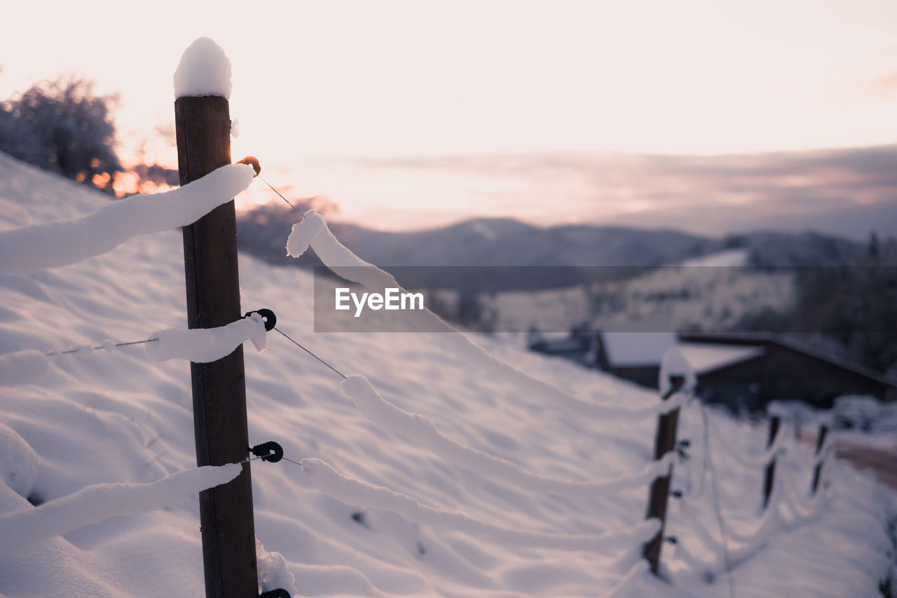 Scenic view of snowcapped mountains against sky during sunset. fence in foreground.