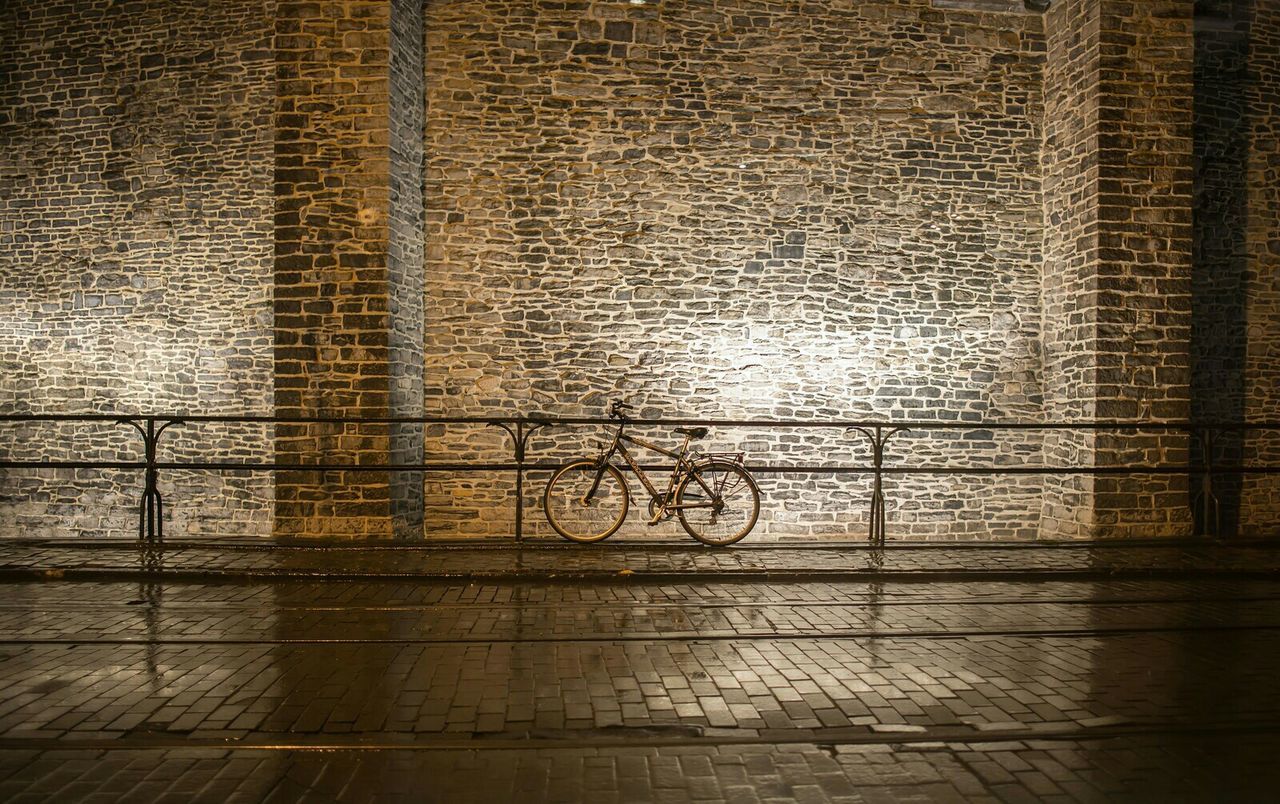 Bicycle parked on wet street by stone wall