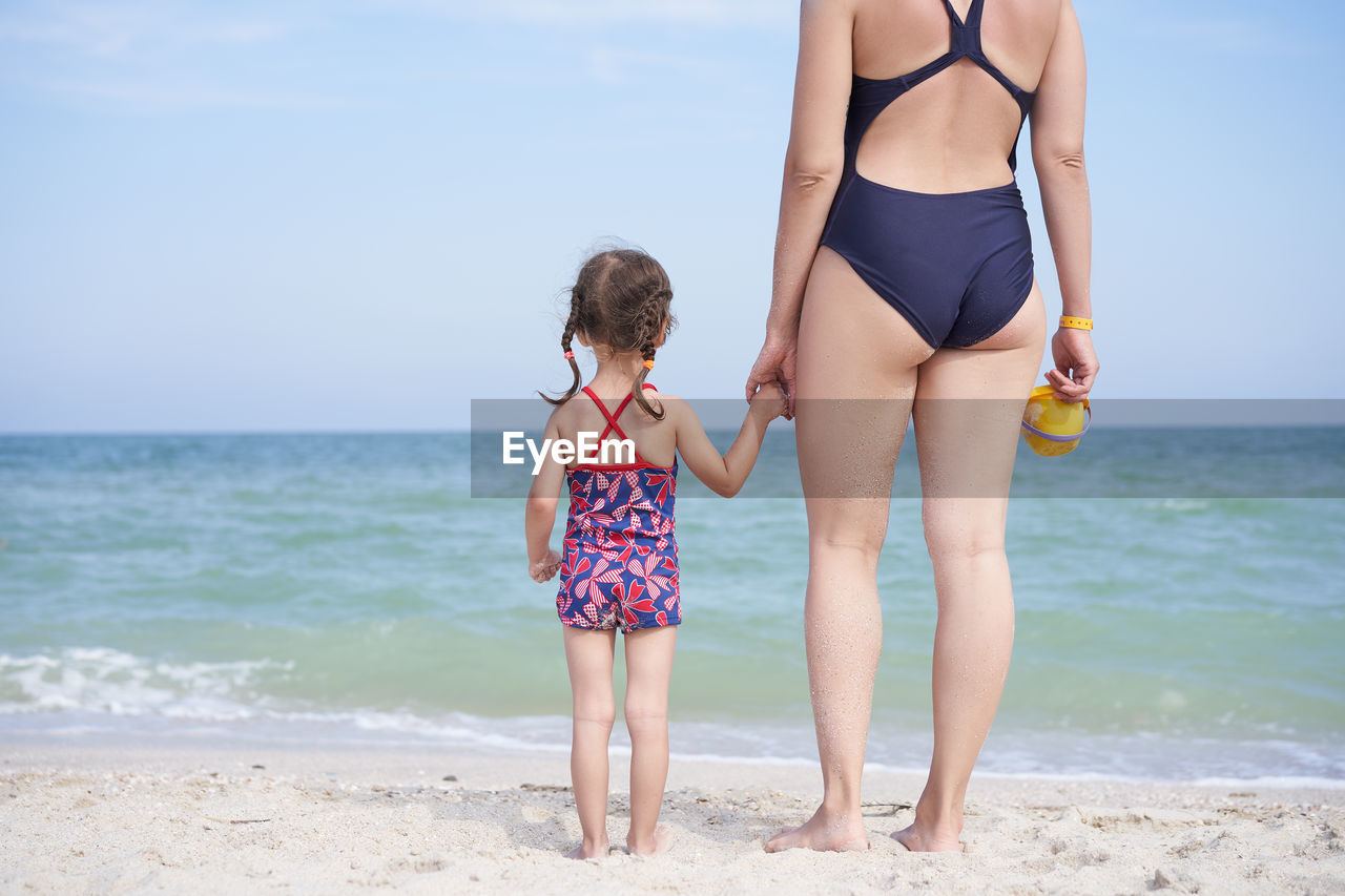 Mother and daughter standing on beach against sky