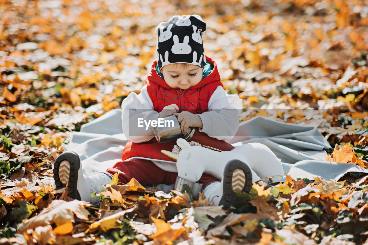 Little cute girl drinks tea from a thermos in the autumn park. cute little toddler baby with