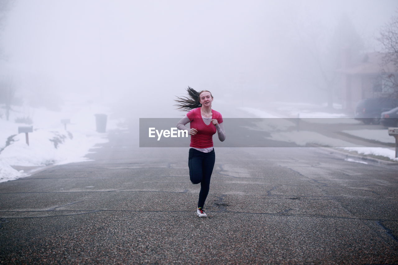 Portrait of smiling young woman running on road during foggy weather