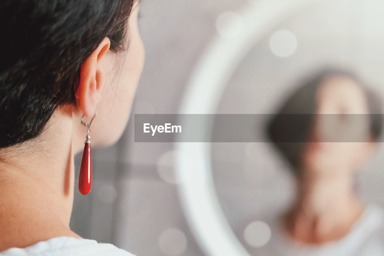 Side view of young woman with red earrings looking at the mirror 