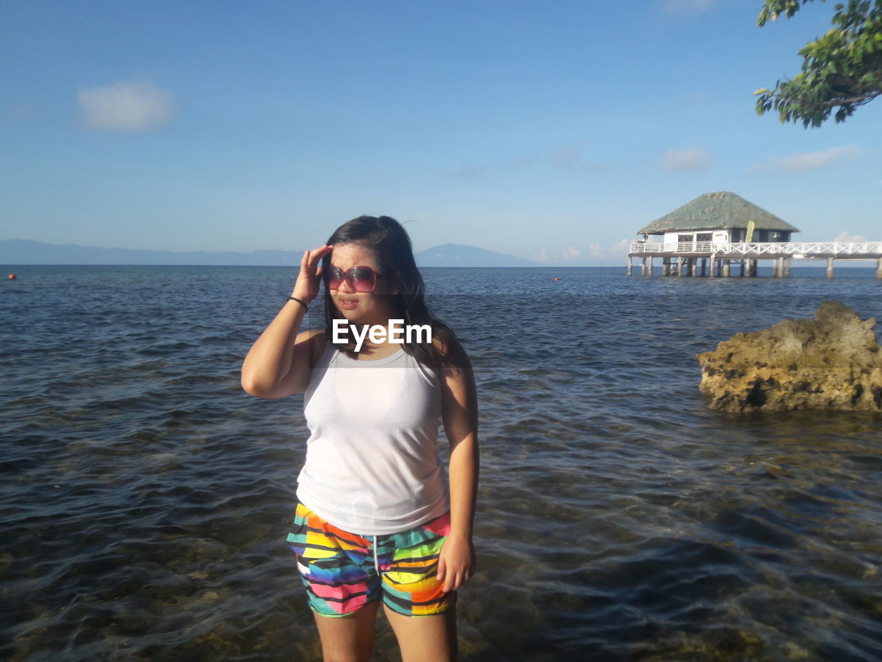 PORTRAIT OF BEAUTIFUL YOUNG WOMAN STANDING ON BEACH