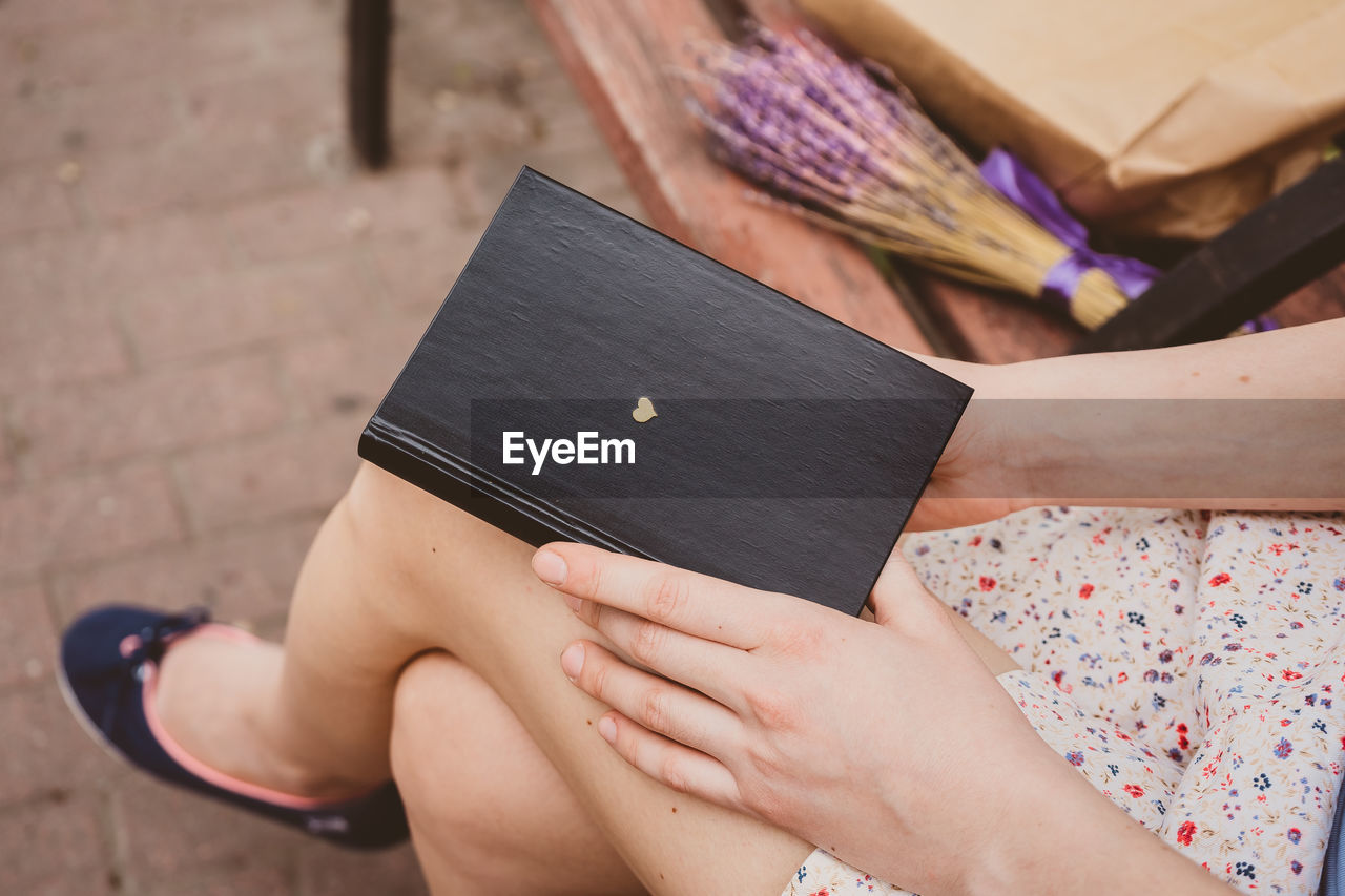 LOW SECTION OF WOMAN SITTING ON BOOK AT HOME