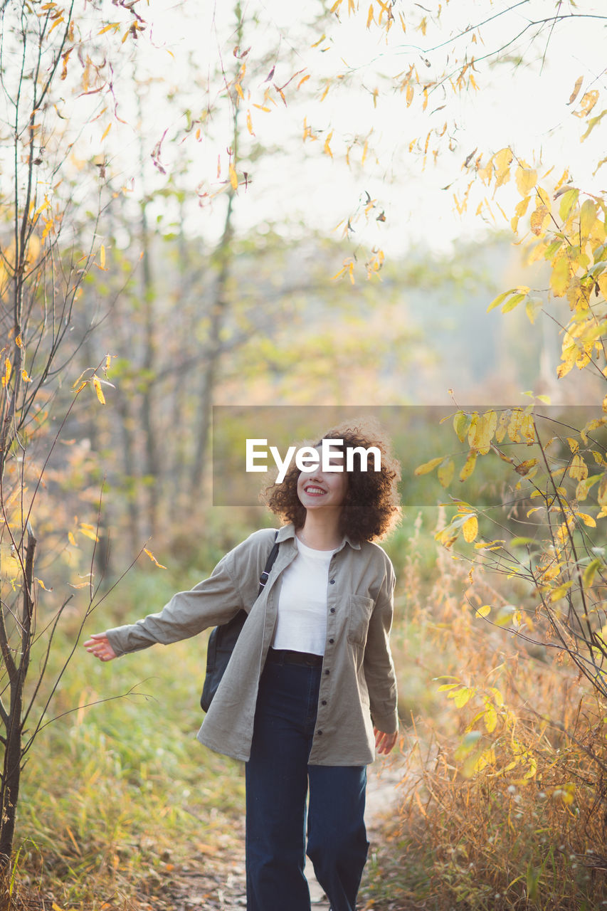 FULL LENGTH PORTRAIT OF SMILING YOUNG WOMAN STANDING ON LAND