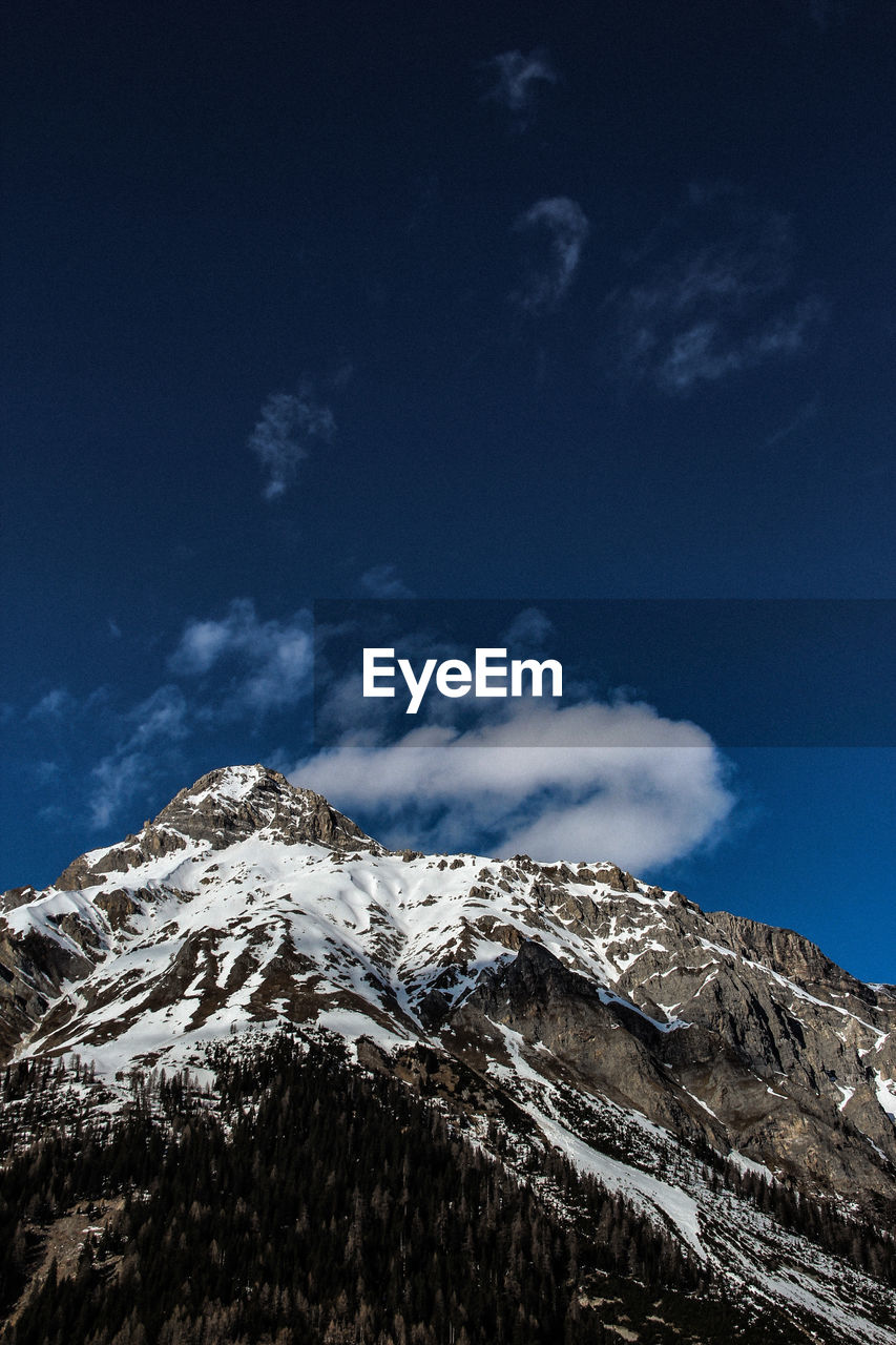 Low angle view of snowcapped mountains against blue sky