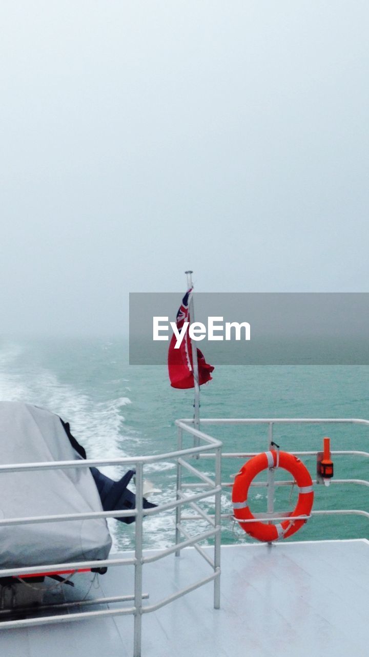 Flag on sailboat sailing in sea against sky during foggy weather