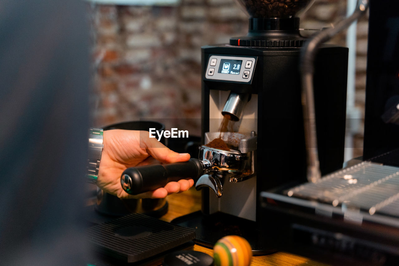 Crop unrecognizable barista pressing coffee in portafilter with tamper while preparing beverage in cafe