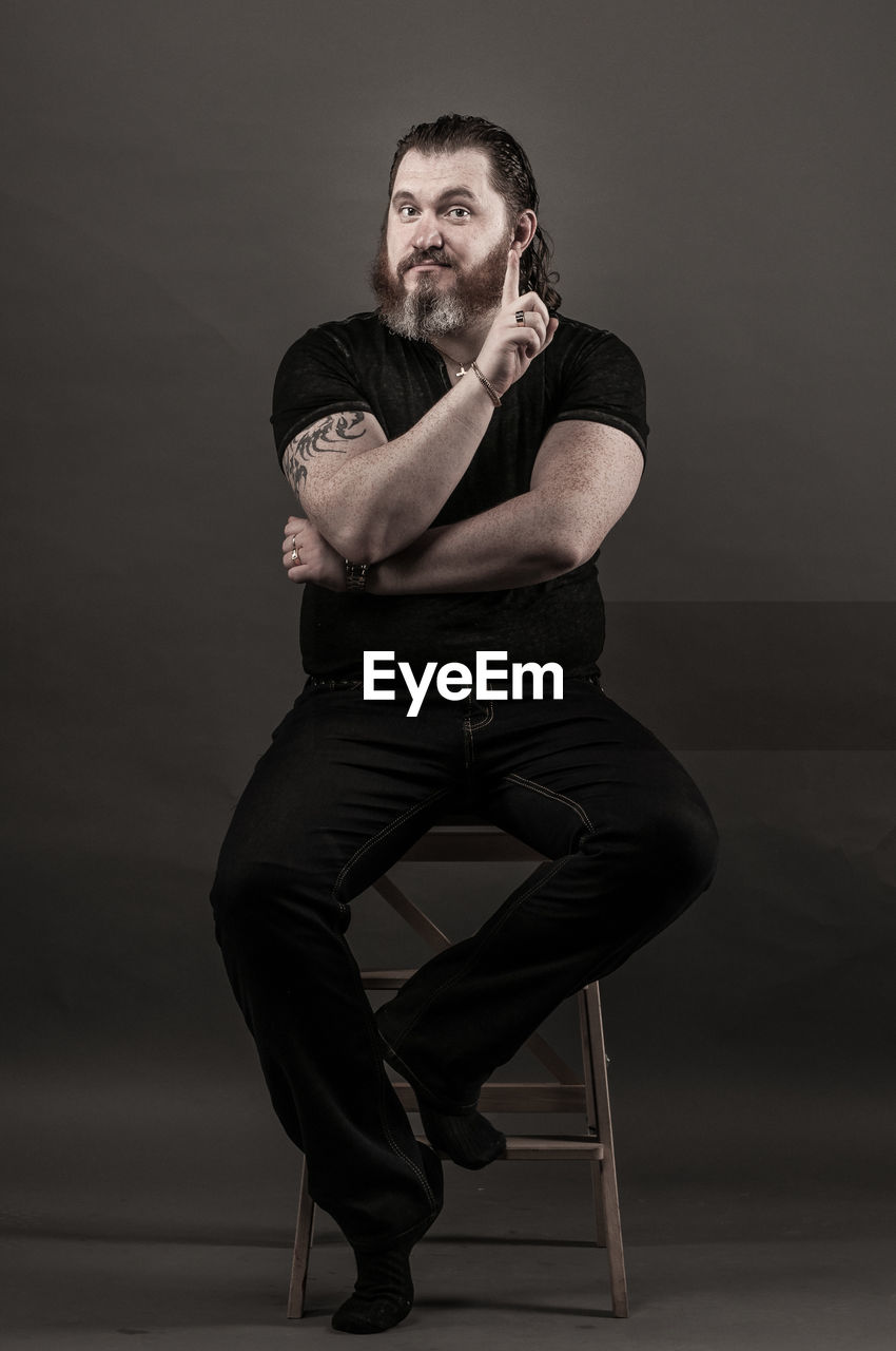 Smiling mid adult man gesturing while sitting against black background