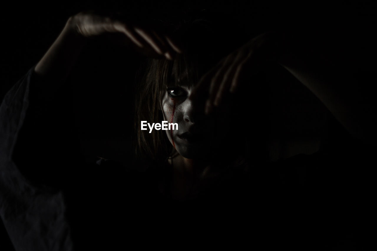 Portrait of young woman with halloween make-up against black background