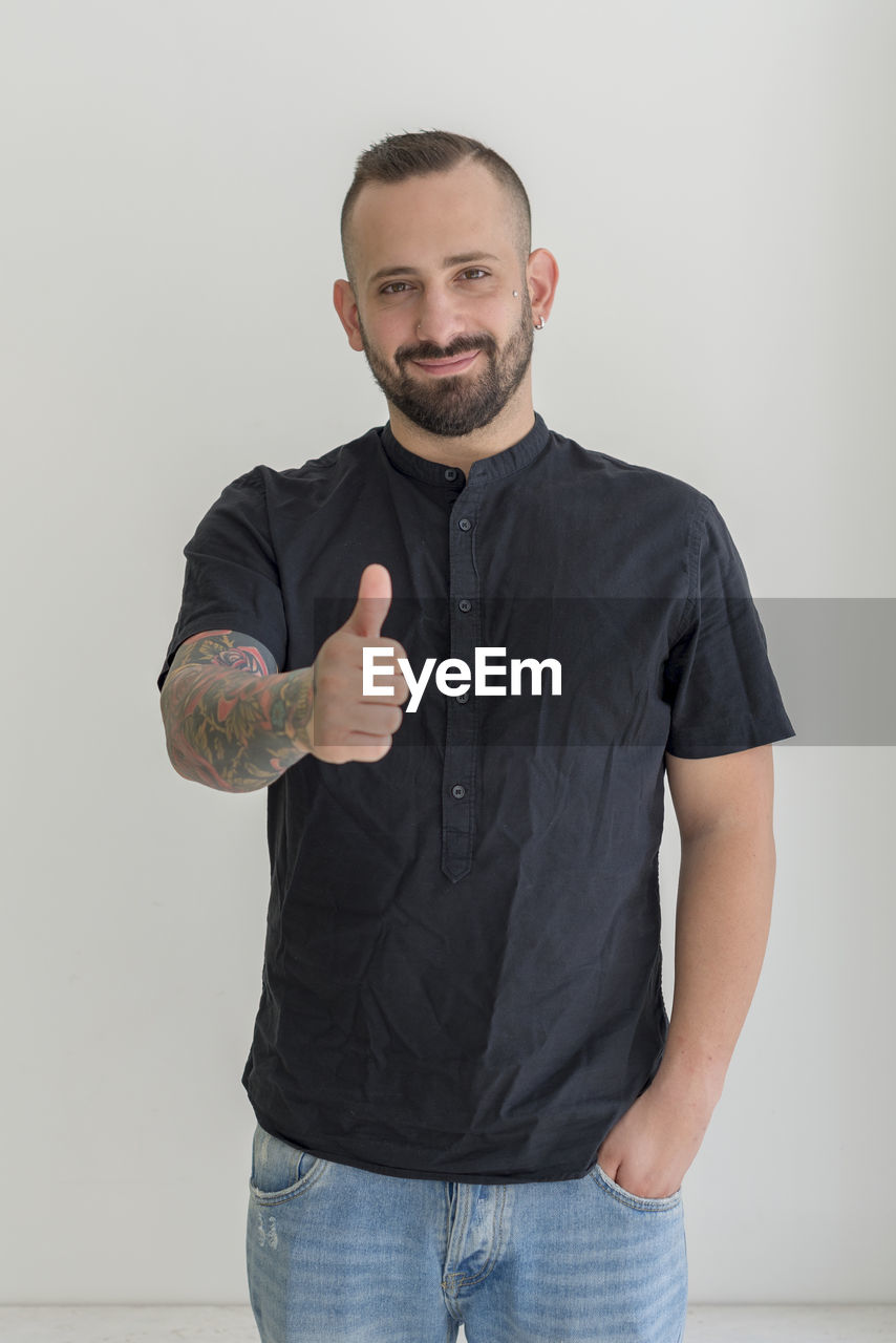 Portrait of young man gesturing thumbs up sign against white background