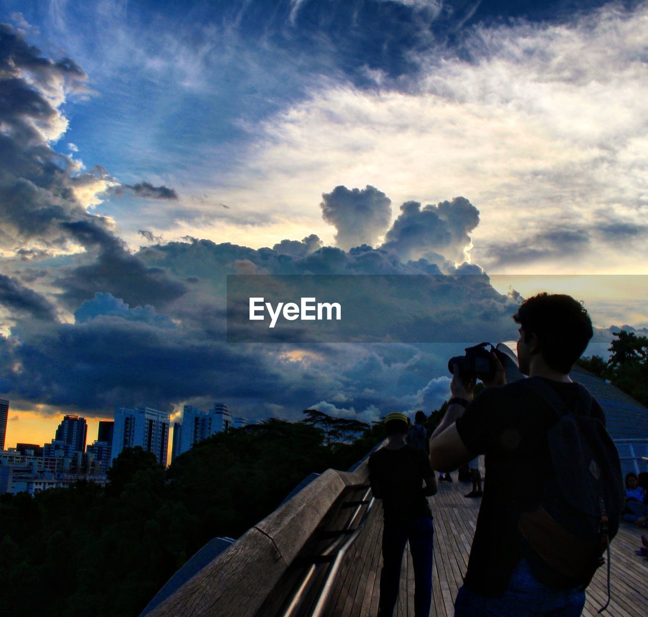 REAR VIEW OF MAN PHOTOGRAPHING AGAINST SKY