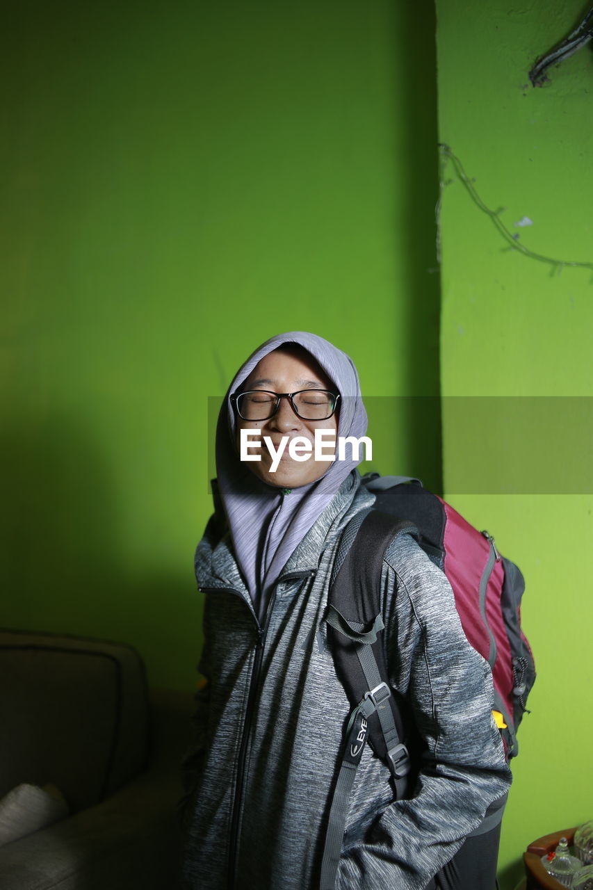 PORTRAIT OF SMILING MID ADULT WOMAN STANDING AGAINST WALL