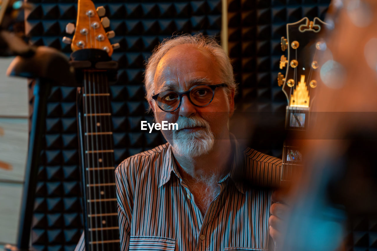 Middle-aged professional guitarist posing in his home recording studio amidst his guitar collection