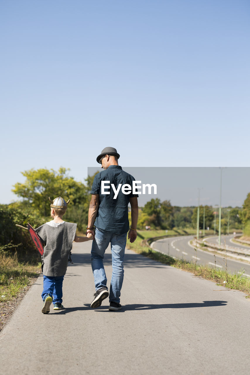 Rear view of father and son walking on road against clear sky