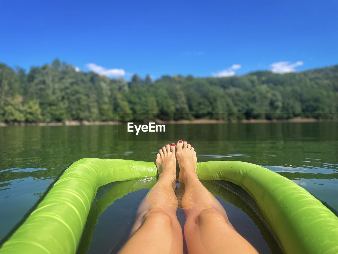 Personal perspective of female tanned legs resting on an inflatable mattress floating on the lake 