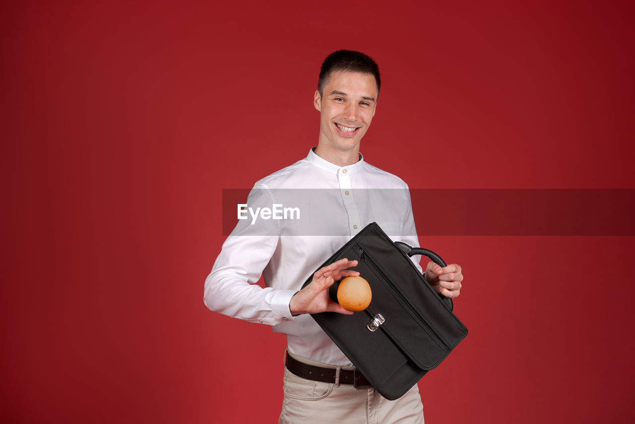 one person, smiling, studio shot, portrait, looking at camera, adult, colored background, happiness, holding, indoors, standing, red, young adult, men, emotion, waist up, business, cheerful, copy space, front view, three quarter length, red background, clothing, occupation, positive emotion