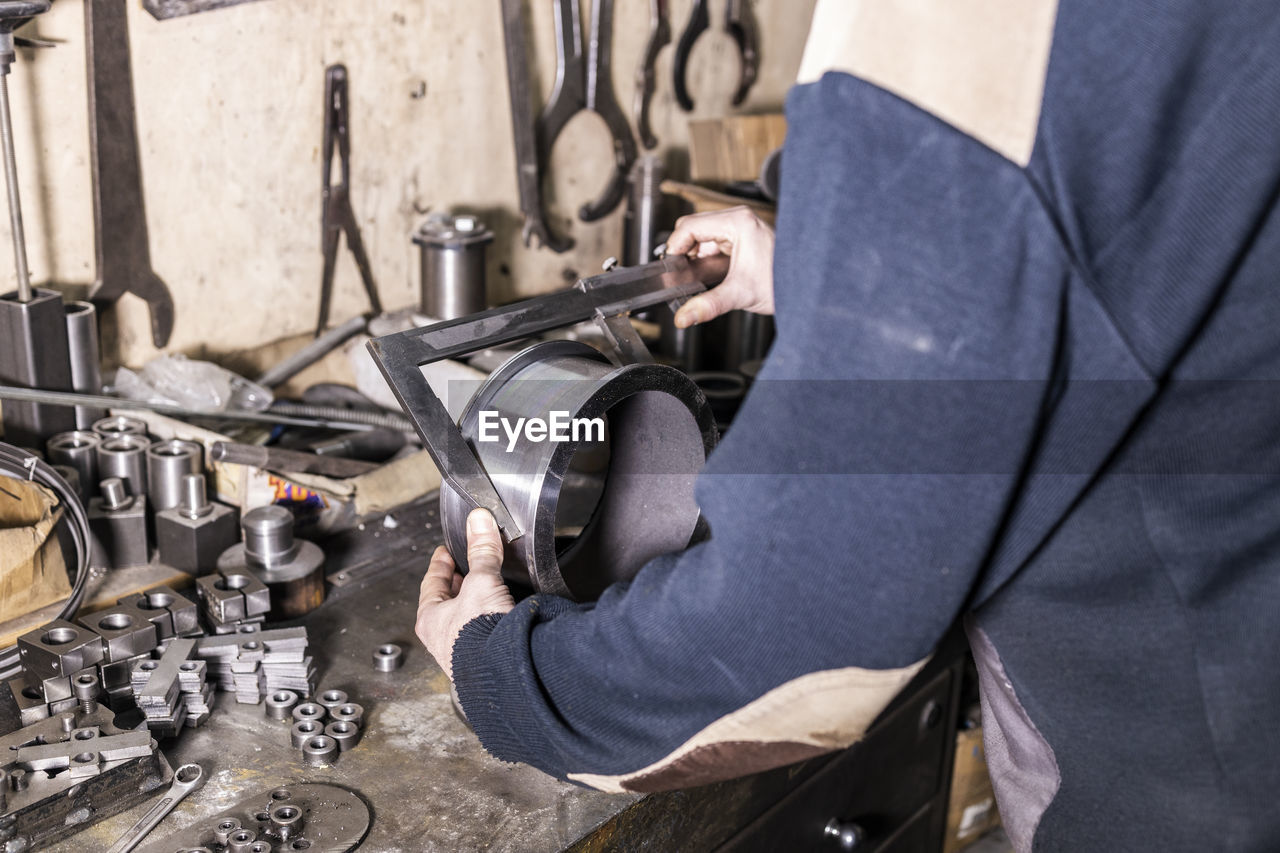 Midsection of worker measuring metal in factory