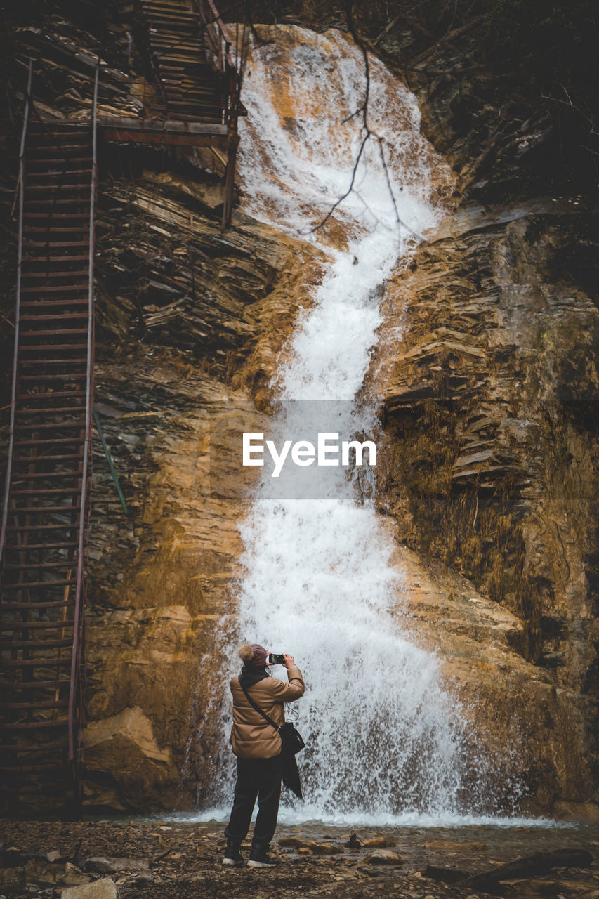 waterfall, one person, water, motion, full length, standing, nature, men, lifestyles, adult, leisure activity, splashing, outdoors, beauty in nature, day, long exposure, young adult, land, sports