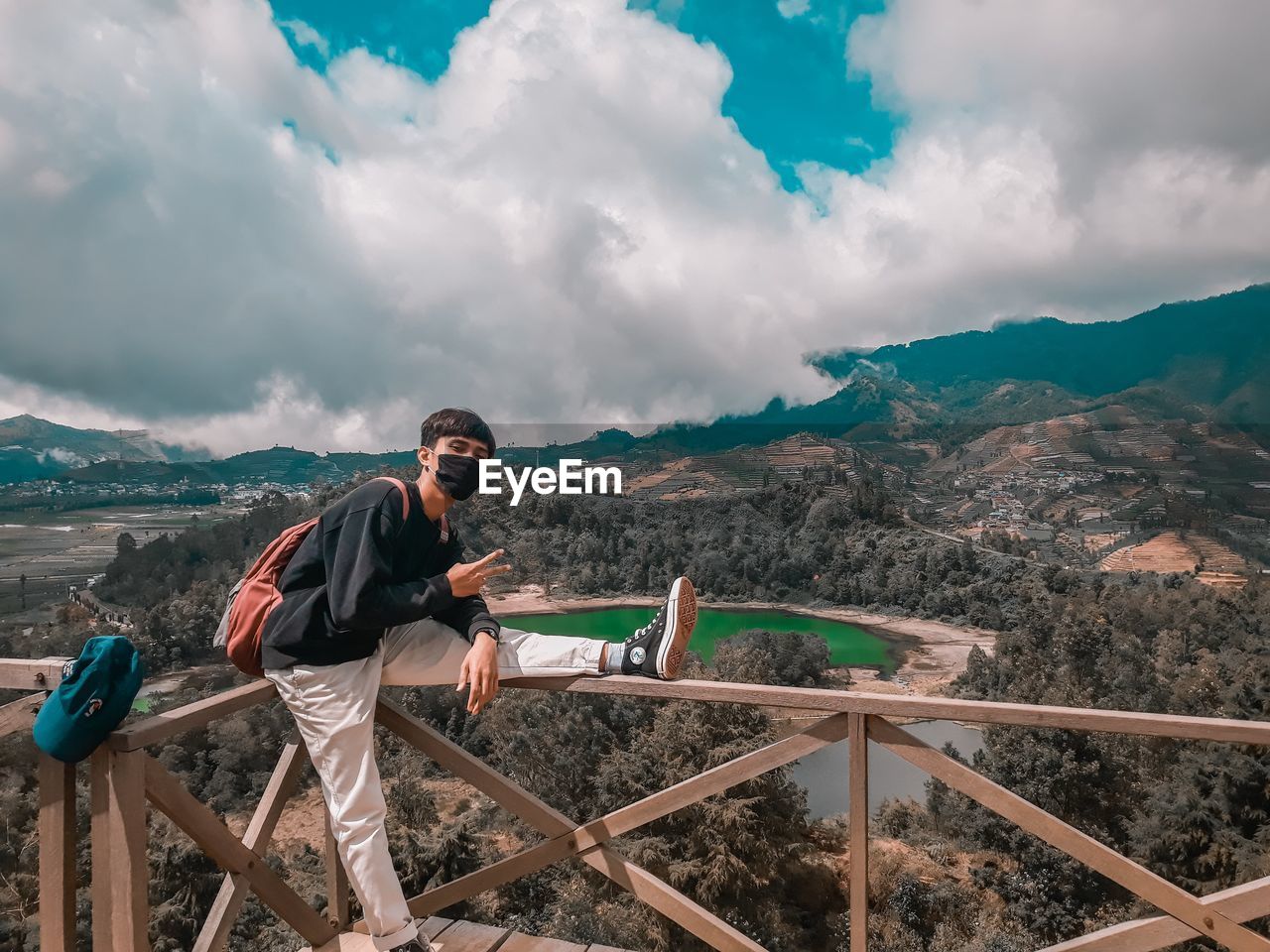 MAN STANDING ON RAILING AGAINST MOUNTAIN