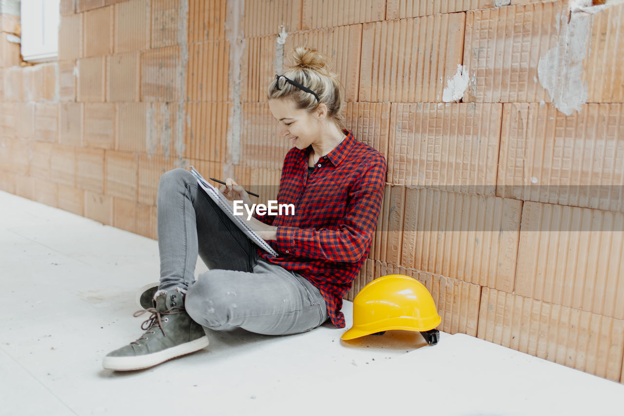 Woman working while sitting against wall