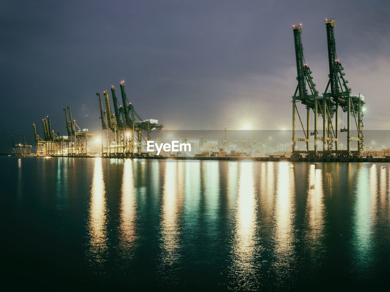 Illuminated harbor by sea against sky at night