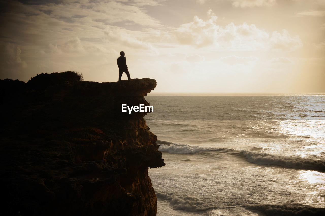 Silhouette man standing on cliff near sea against sky during sunset