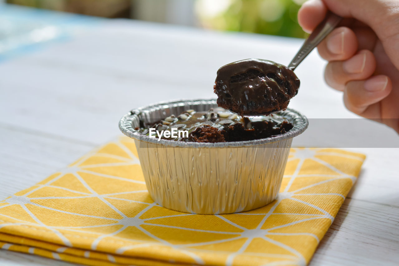 Eatting dark chocolate cake with chocolate chip topping in foil cup.