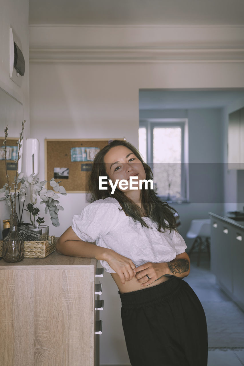 Smiling woman leaning on cabinet at home