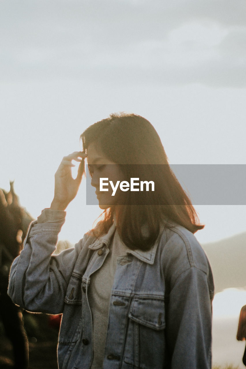 Woman looking down while standing against sky