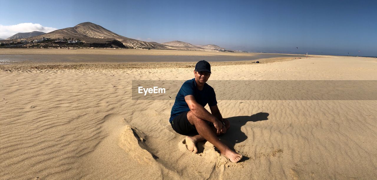 Full length of young man sitting on sand at beach