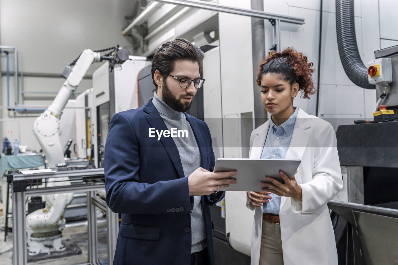 Young businessman with colleague discussing over tablet pc in factory