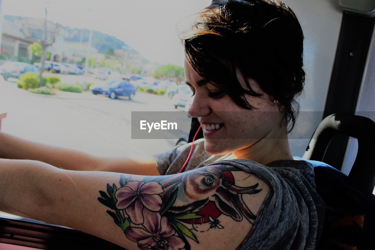 Smiling young woman with floral tattoo on arm traveling in bus