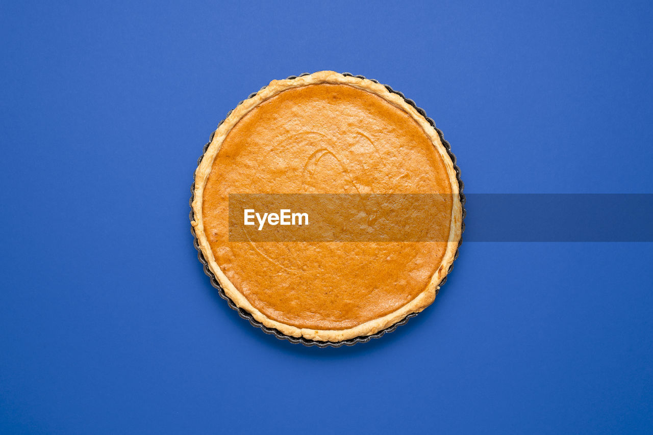 Above view, a homemade pumpkin pie isolated on a dark blue background. pie in metal tray top view.