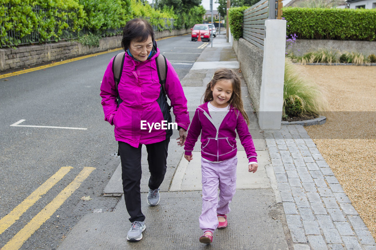 Full length of grandmother and granddaughter walking at sidewalk in city