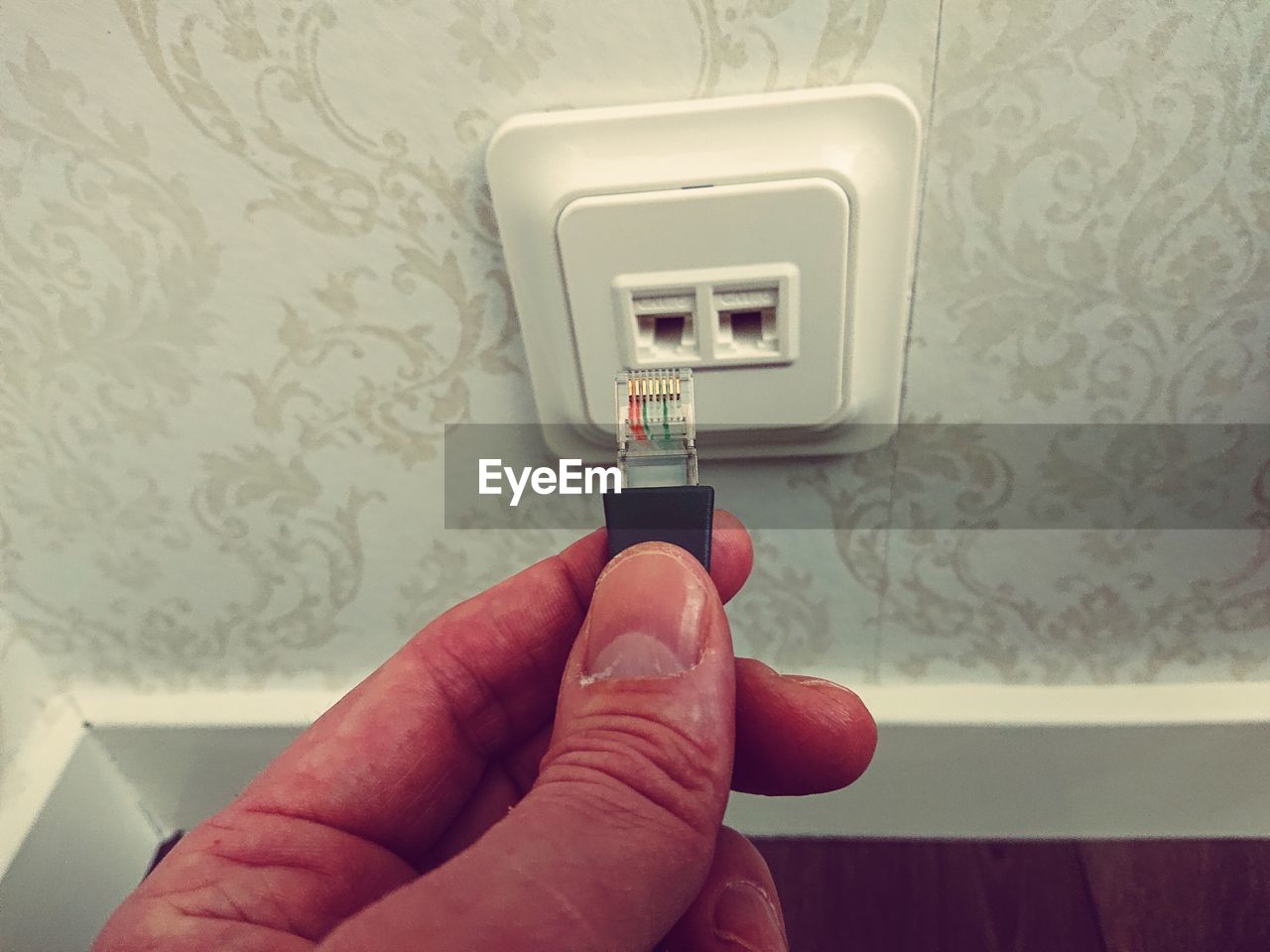 Close-up of hand holding network connection plug against wall