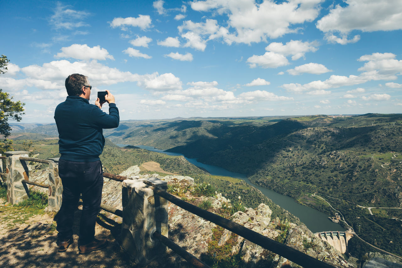 Rear view of man photographing mountains against sky