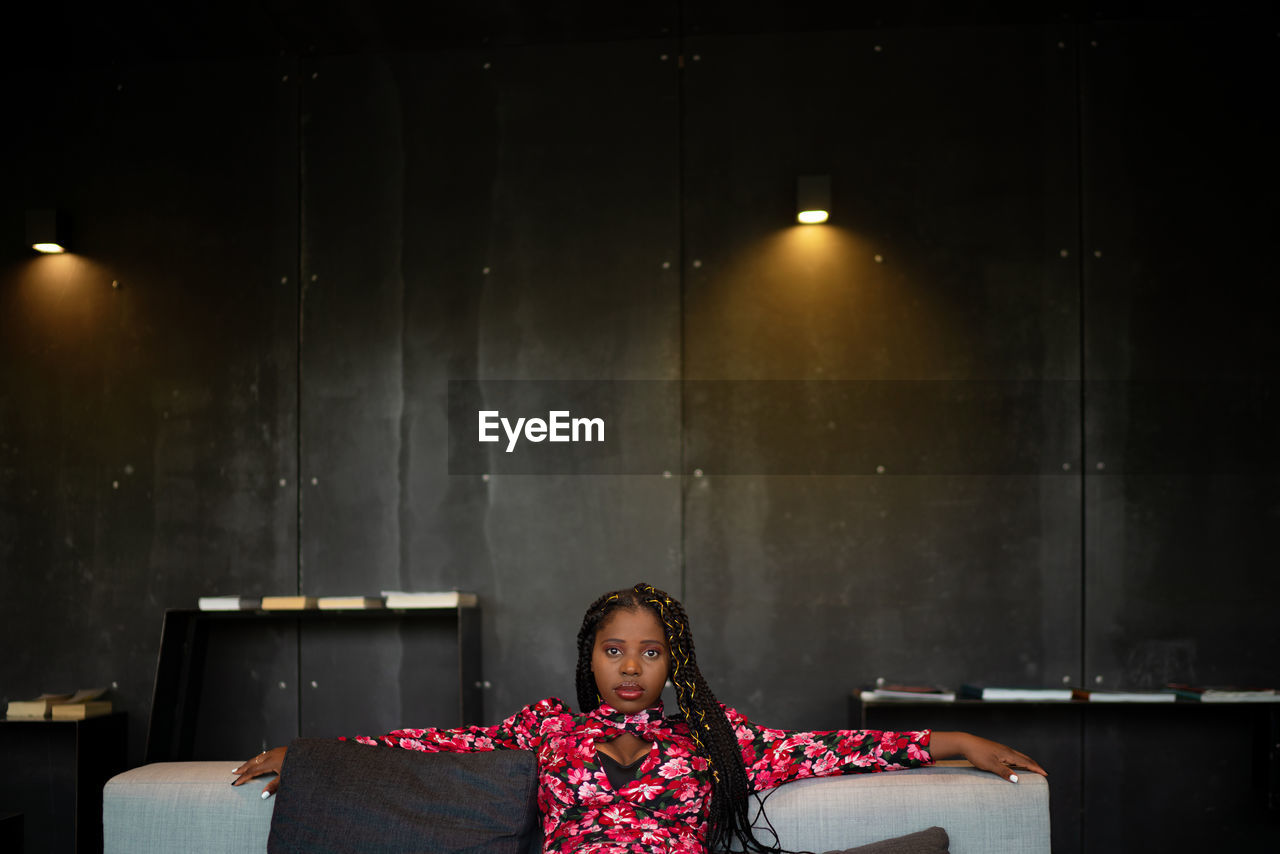 African american female in bright pink dress sitting on couch in hotel lobby and looking at camera