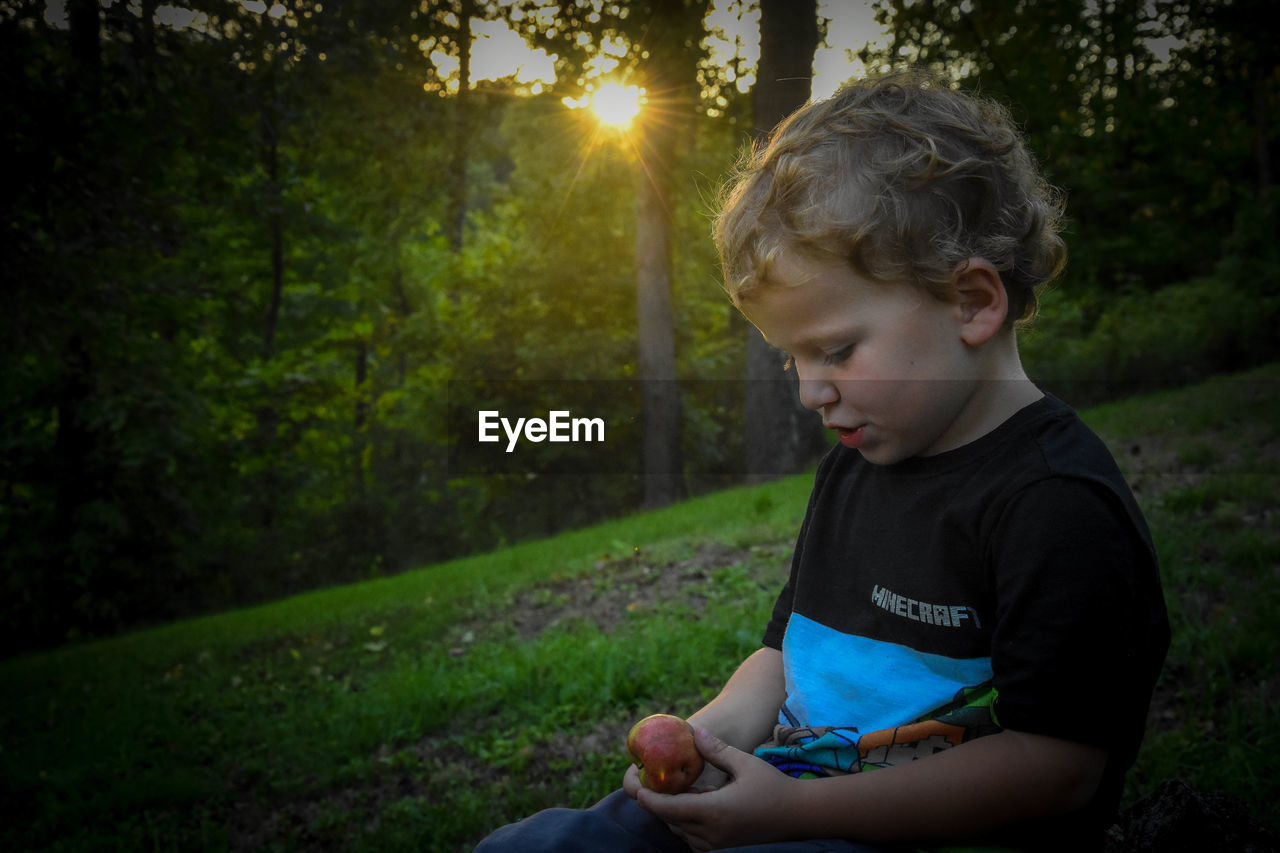 BOY LOOKING AT CAMERA WHILE SITTING ON LAND