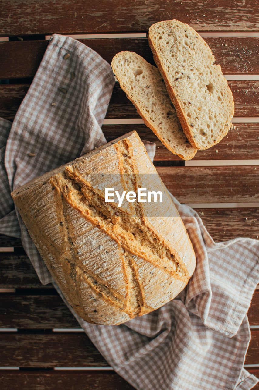 Top view of freshly baked bread loaf on rustic wooden cutting board and napkin