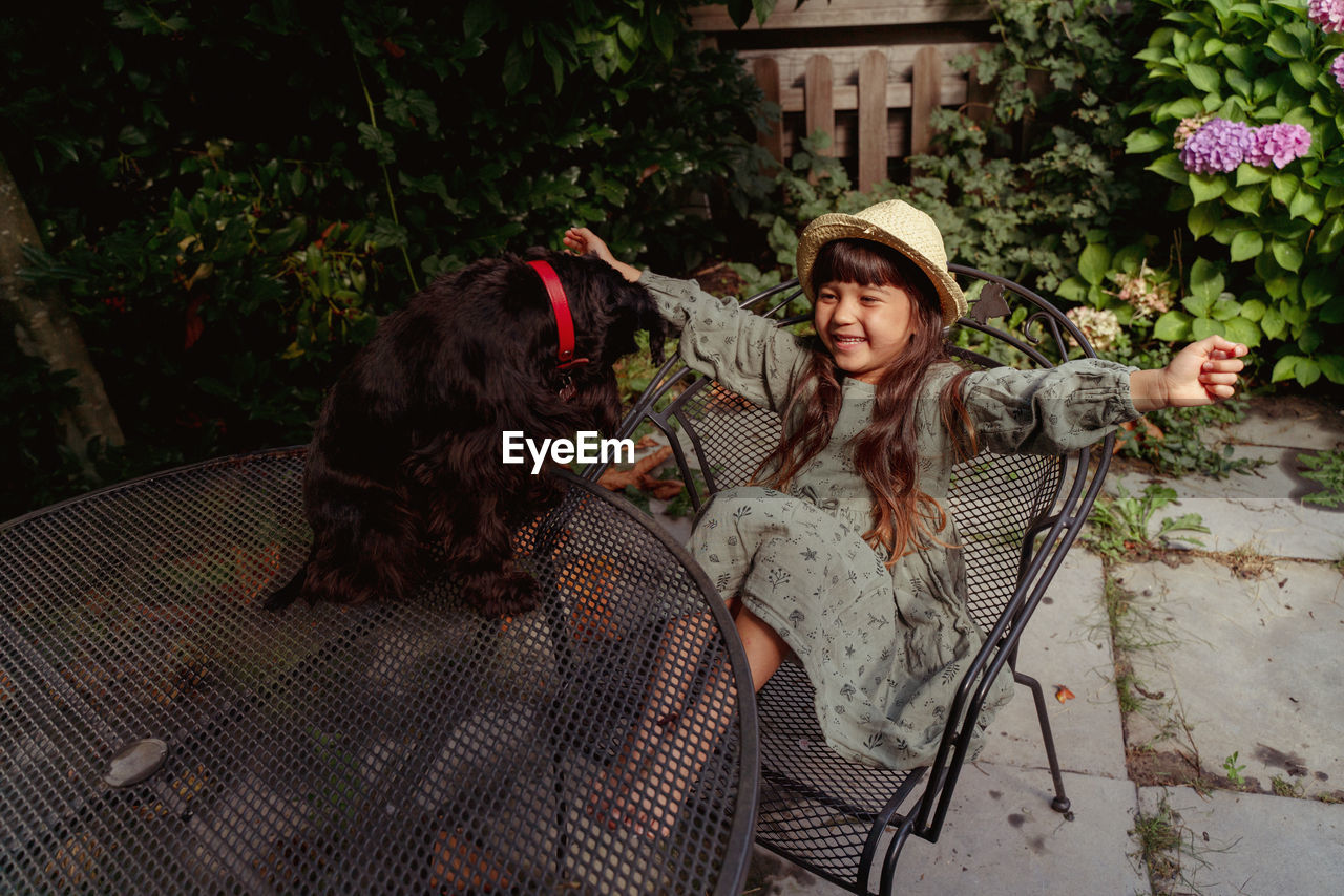 Portrait of girl sitting on chair with black little dog