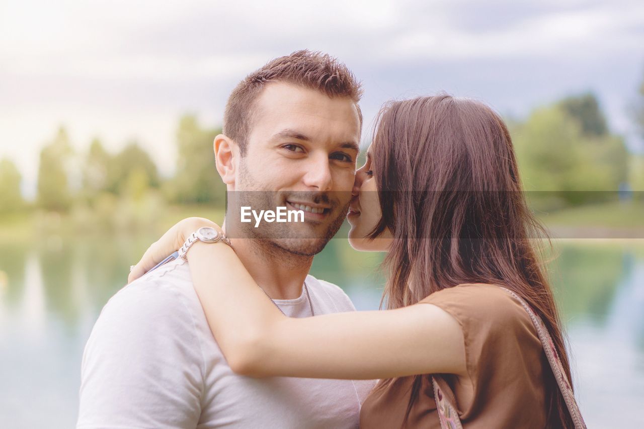 Portrait of smiling boyfriend with loving girlfriend against lake