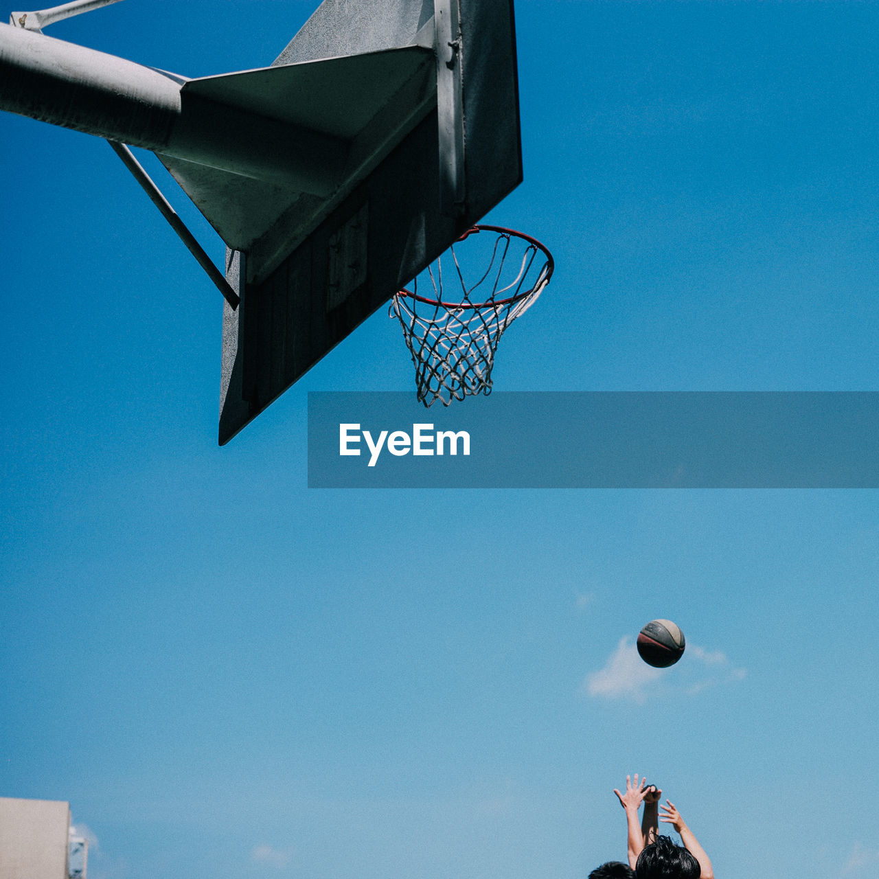 Low angle view of people playing basketball against blue sky