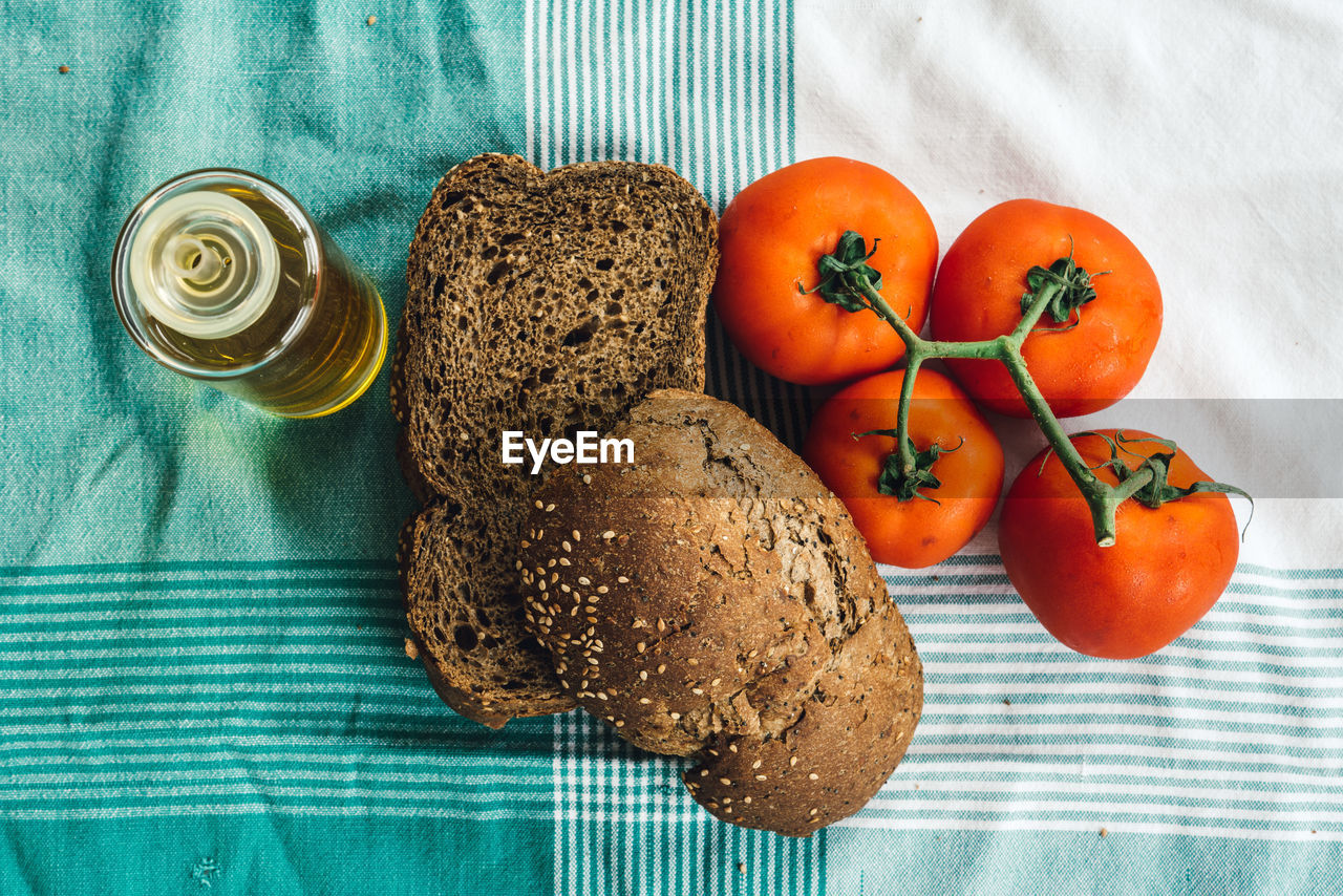 Directly above shot of brown bread with olive oil bottle and tomatoes on tablecloth at table