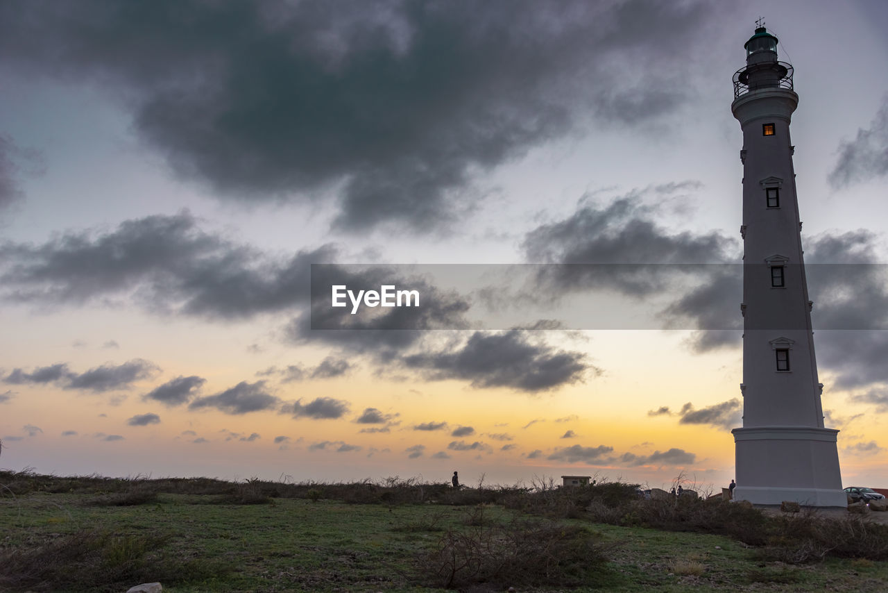 LIGHTHOUSE AMIDST BUILDINGS AGAINST SKY AT SUNSET