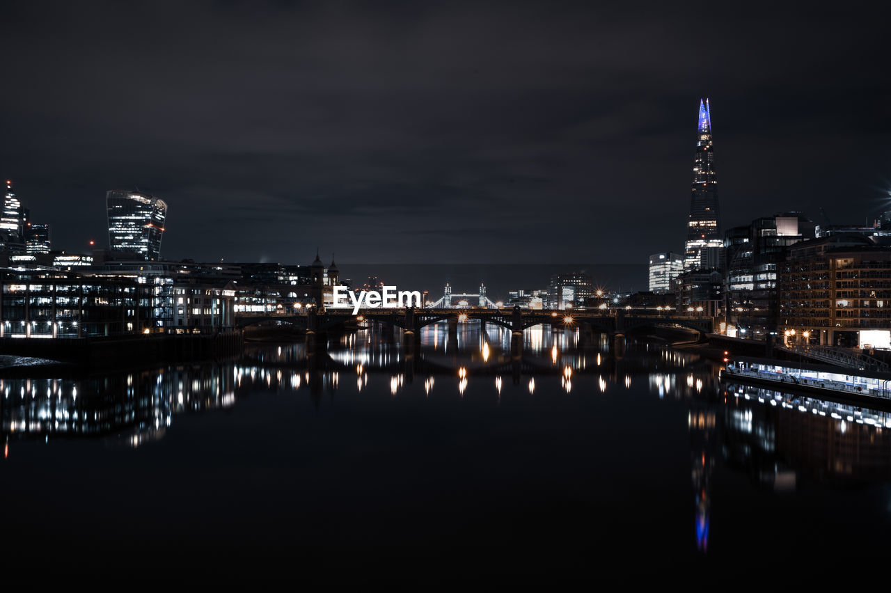 ILLUMINATED BUILDINGS BY RIVER AGAINST SKY