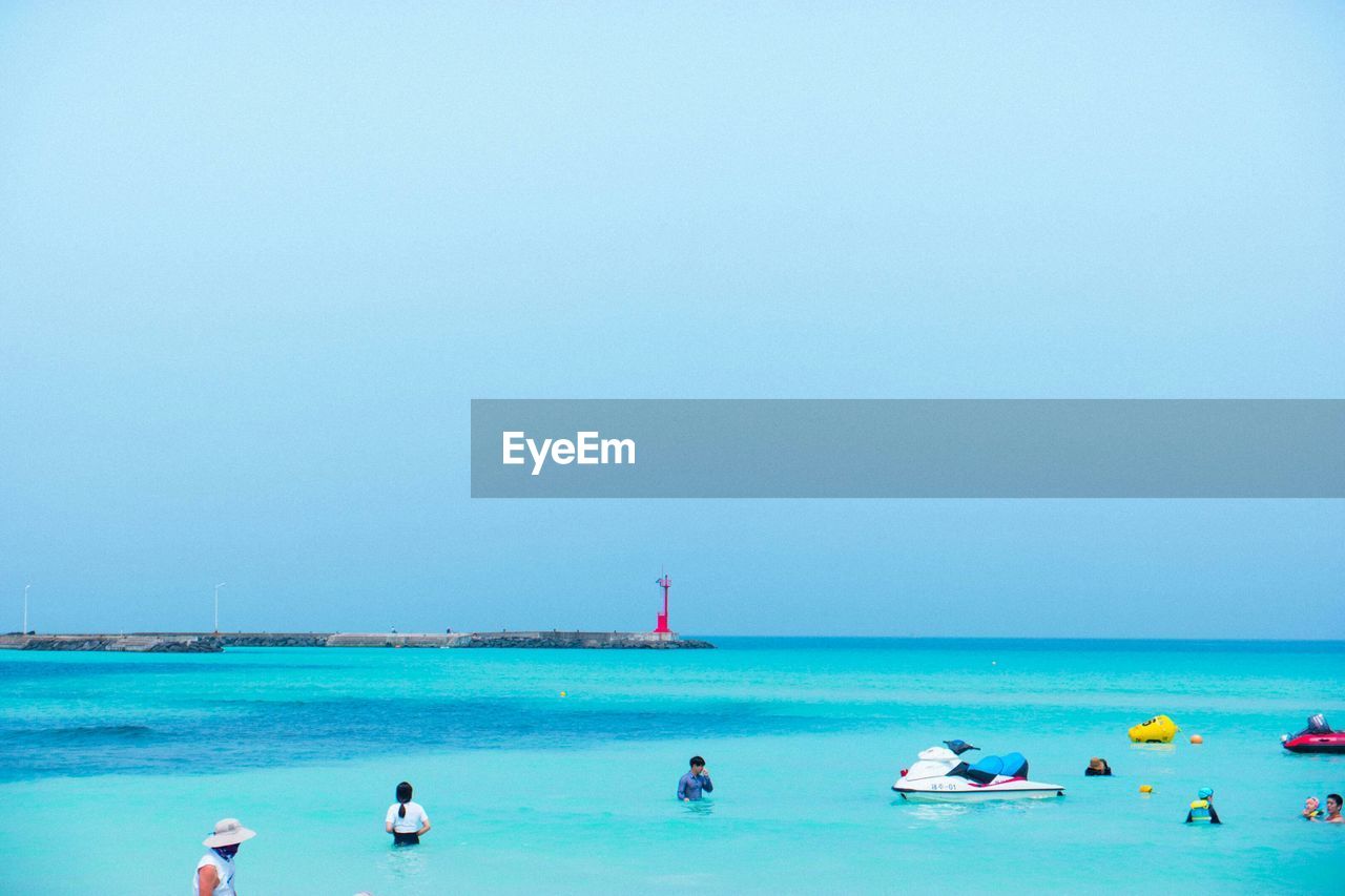 People at beach against clear blue sky