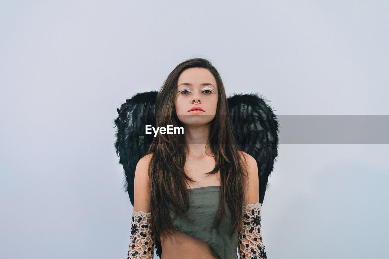 Portrait of beautiful young woman wearing wings against white background